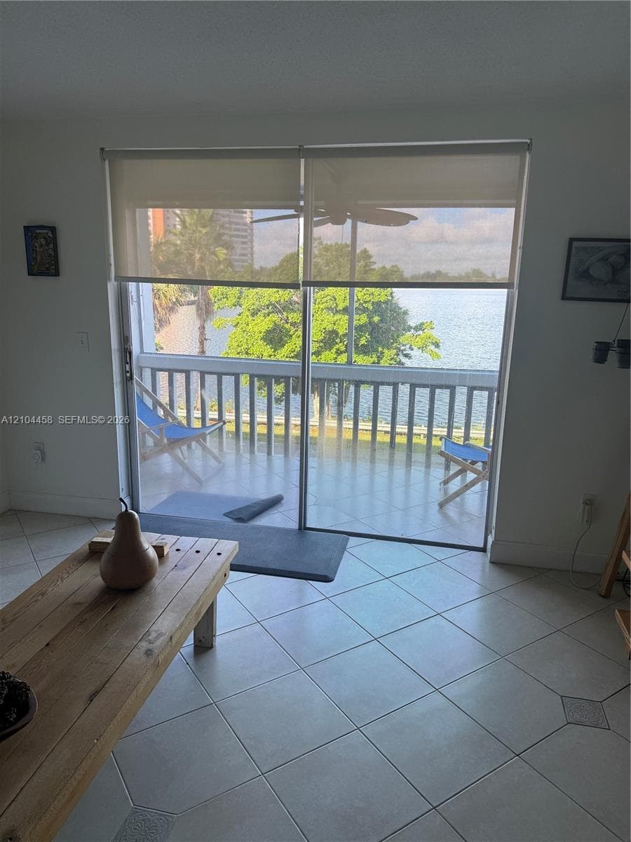 Sliding glass doors opening to a balcony with metal railings, tile flooring, and water frontage