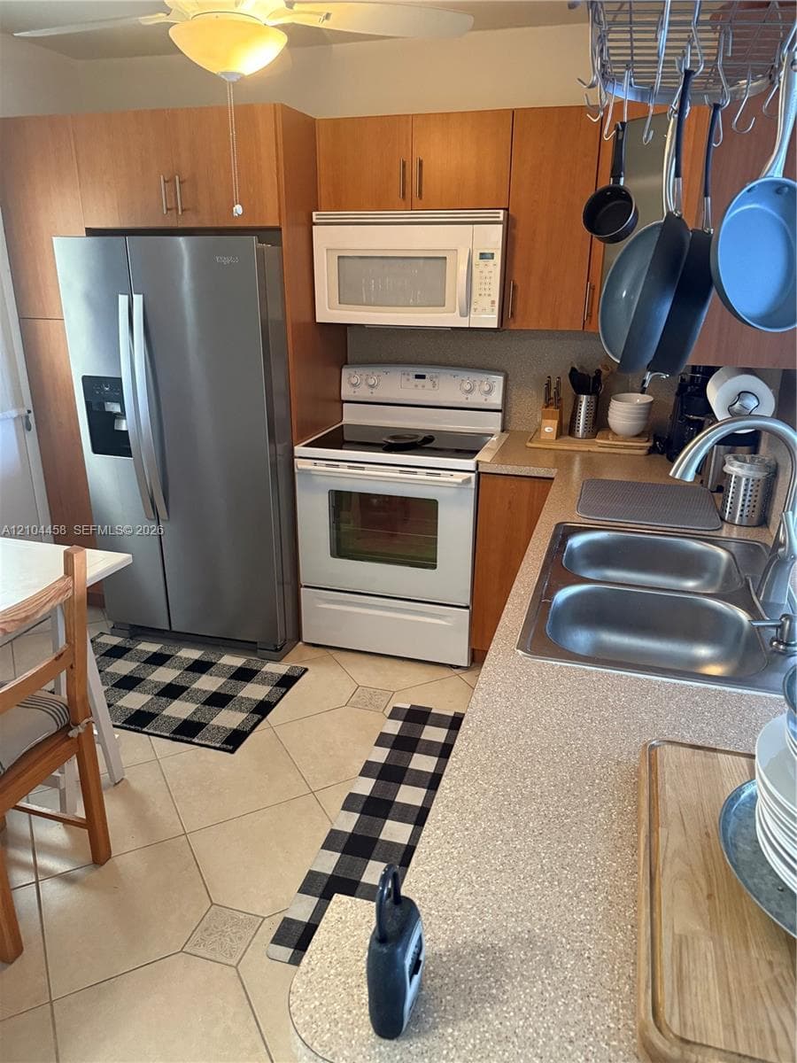 Kitchen featuring wood-finish cabinetry, stainless steel side-by-side refrigerator, white electric range, over-the-range microwave, and dual-basin stainless steel sink with arch faucet