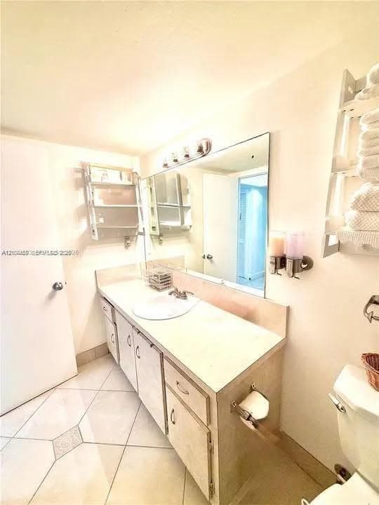 Bathroom featuring an extended vanity with stone-surfaced countertop, integrated basin, large wall-mounted mirror, overhead lighting, and ceramic tile flooring