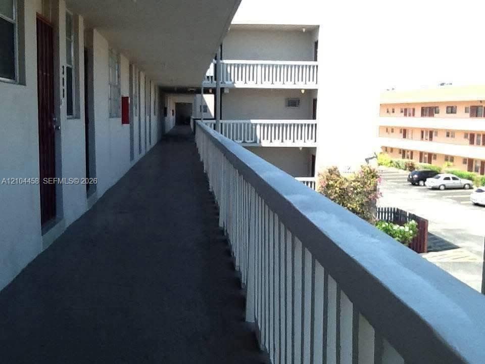 Exterior covered walkway featuring white metal railings and painted concrete surfacing