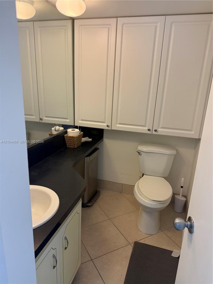 Vanity featuring a dark countertop, white cabinetry, a recessed sink, wall-mounted upper storage cabinets, and tile flooring