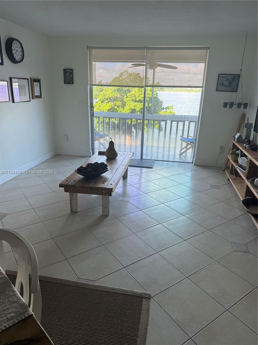 Large-format ceramic tile flooring, sliding glass door with roller shade, and attached balcony featuring a water backdrop