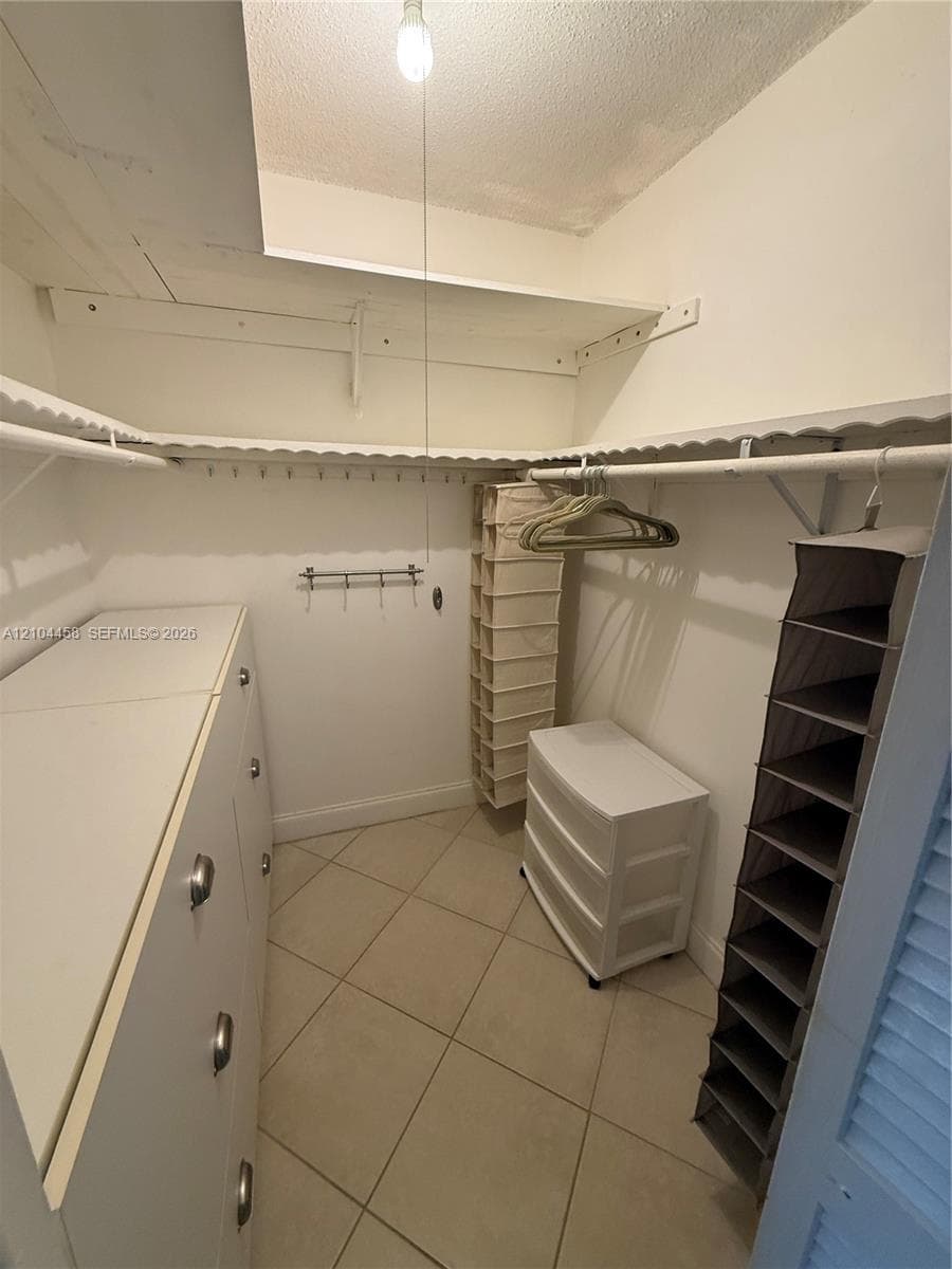 Walk-in closet featuring white built-in cabinetry, ceramic tile flooring, and integrated white shelving