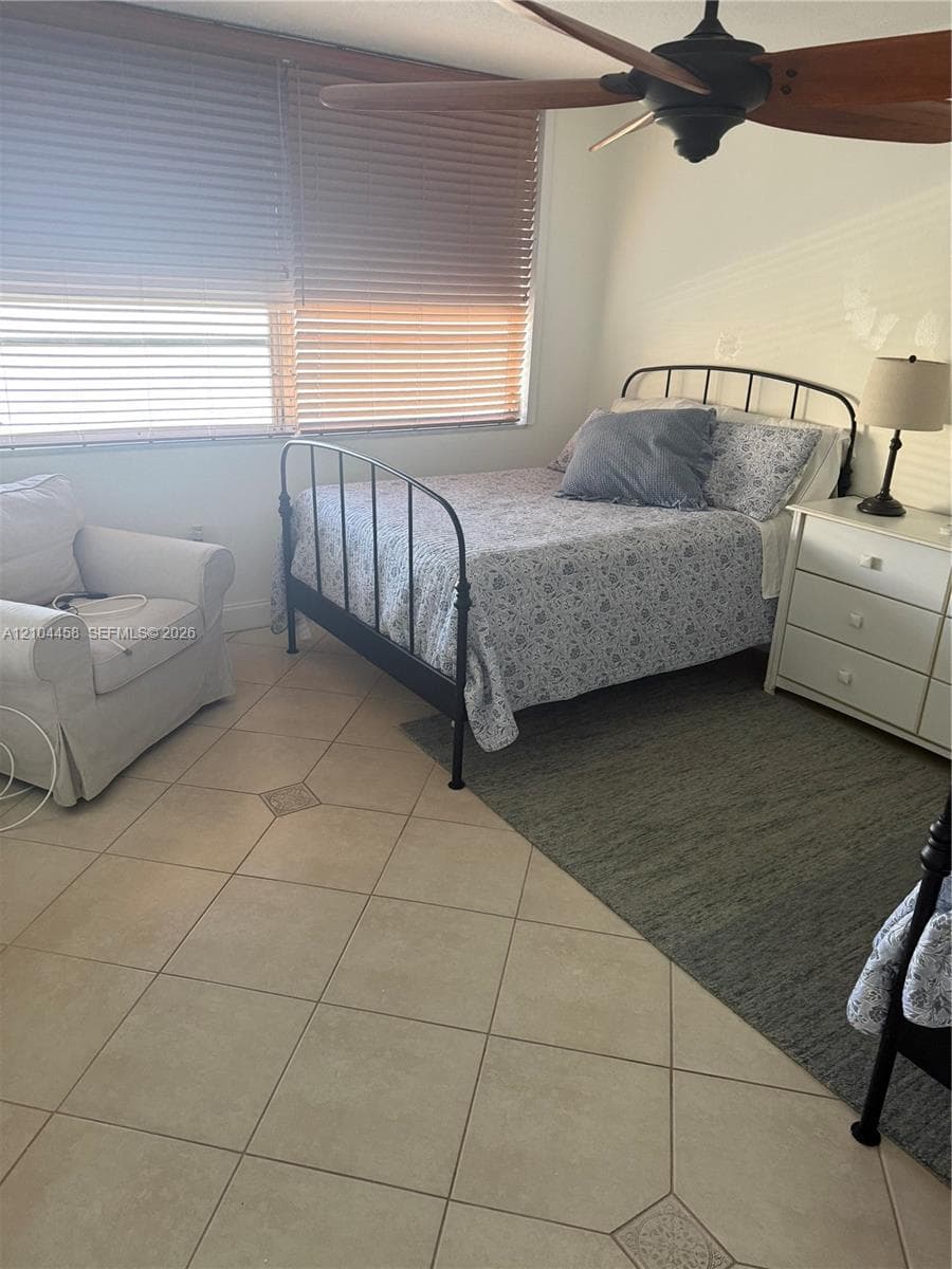 Large-format tile flooring, multi-pane window with horizontal blinds, and a ceiling-mounted fan with wood-finish blades