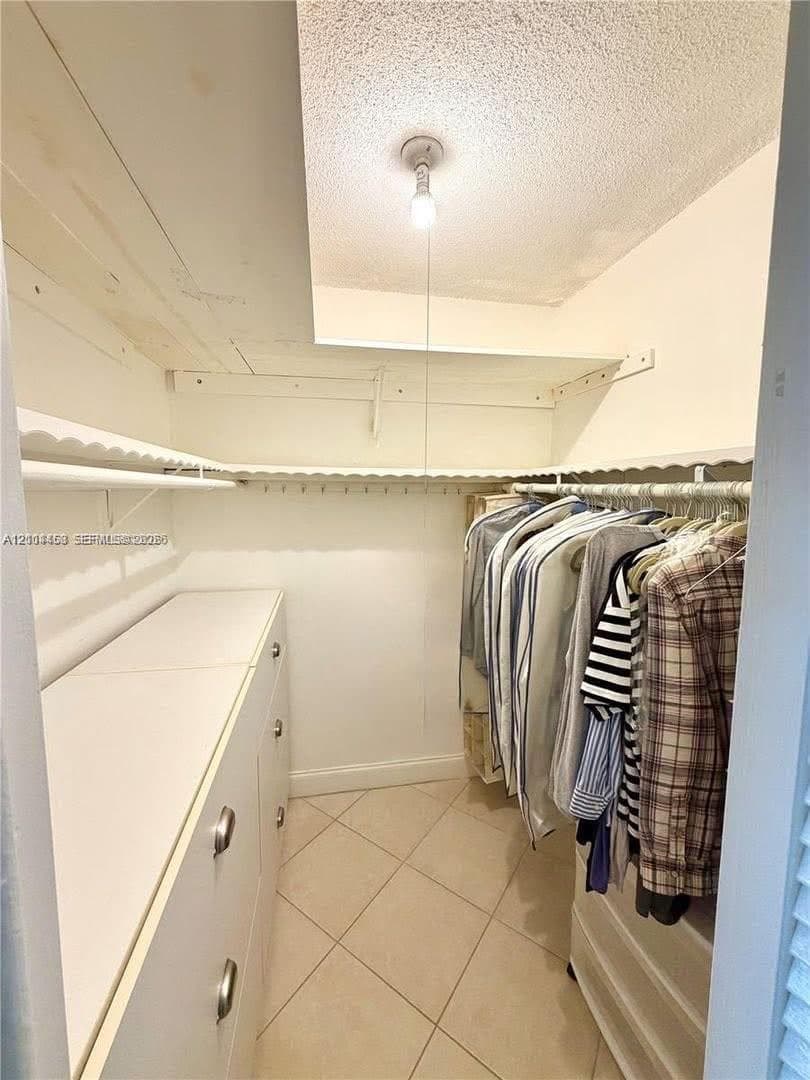 Storage space featuring built-in cabinetry, upper shelving with integrated hanging rods, and tile flooring