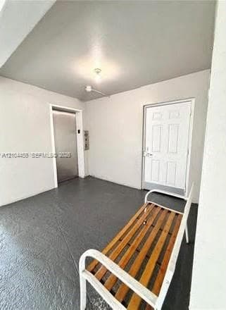 Foyer area featuring a textured gray floor finish, stainless steel elevator doors, and a paneled entry door