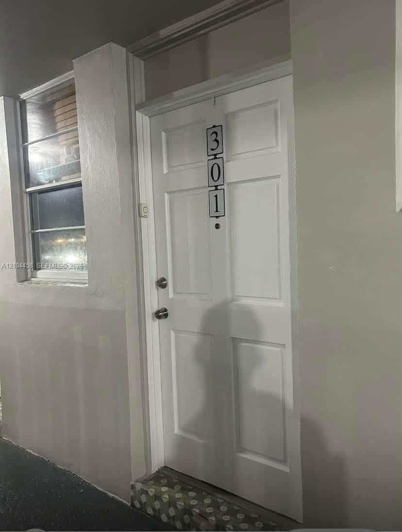 White four-panel entry door with integrated door knocker, door viewer, and metallic hardware, featuring a transom window above and a multi-pane window