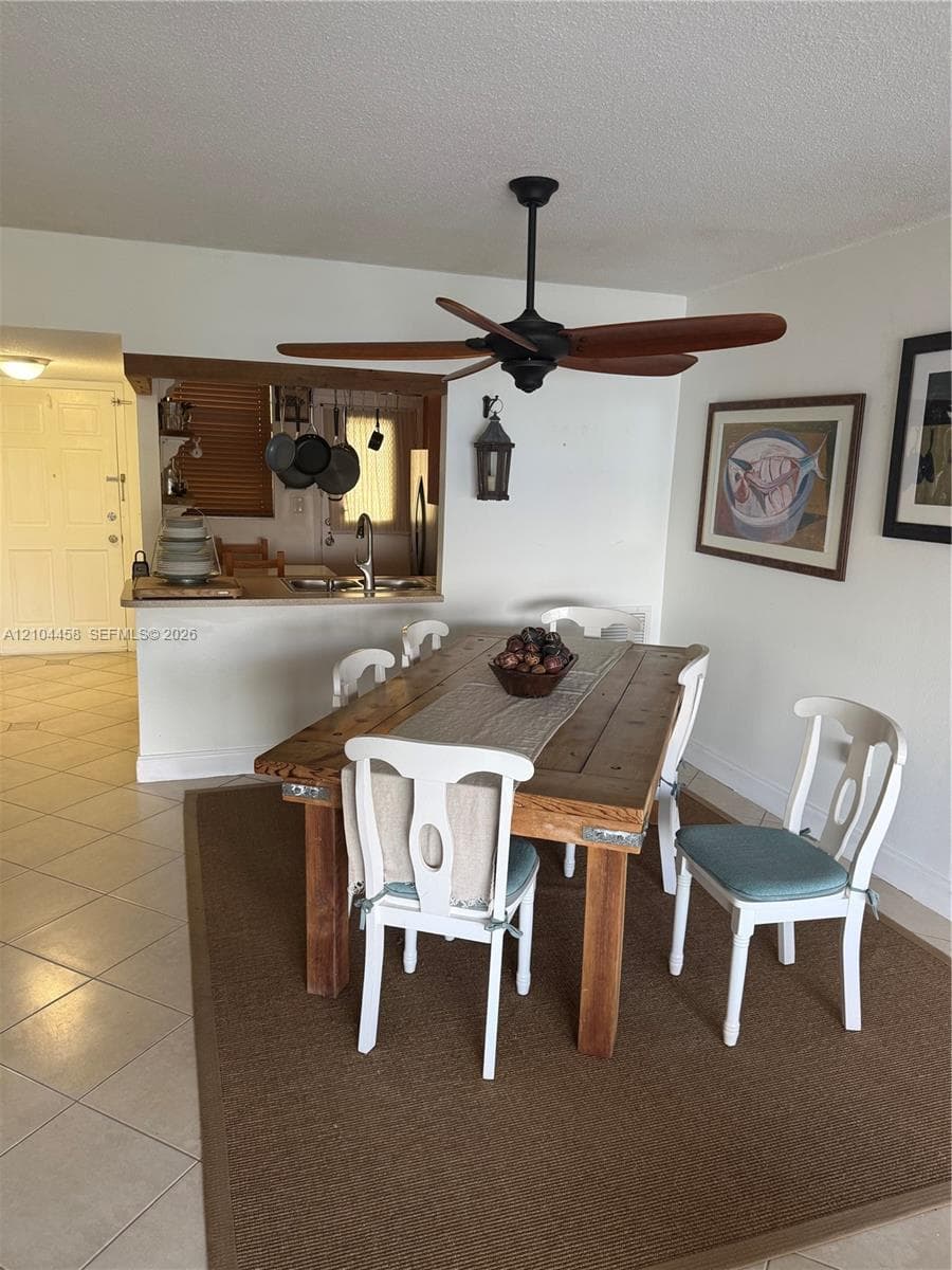 Open-concept area featuring a matte black ceiling fan with wooden blades, neutral ceramic tile flooring, and a pass-through opening with a stone-surface counter
