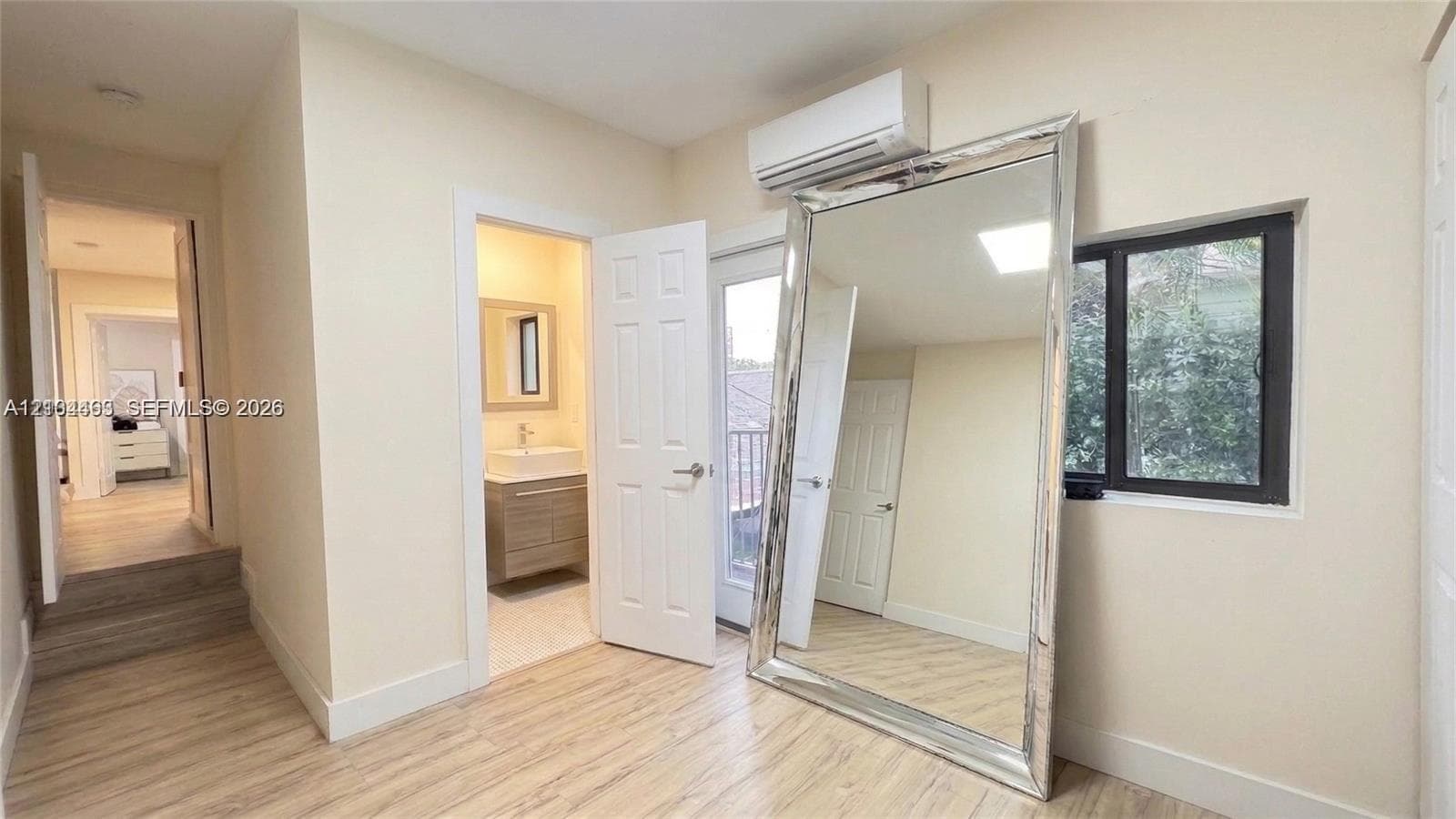 Interior featuring light-toned wood-finish flooring, a wall-mounted ductless air conditioning unit, and a window with a dark frame