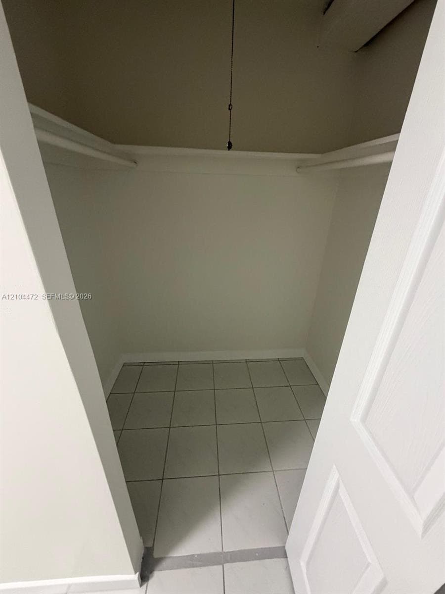 Storage closet featuring neutral floor tiling, built-in shelving, and a ceiling-mounted light fixture
