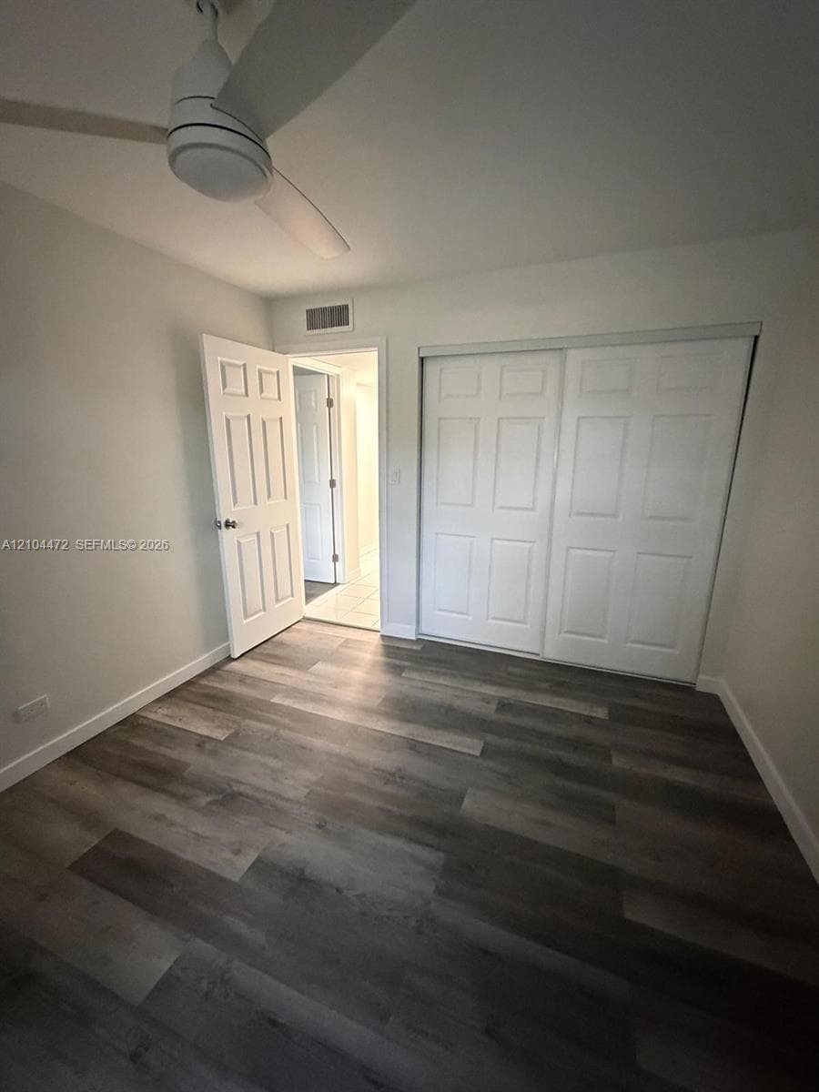 Room featuring wood-finish flooring, a white ceiling fan, and a built-in sliding-door closet with six-panel doors