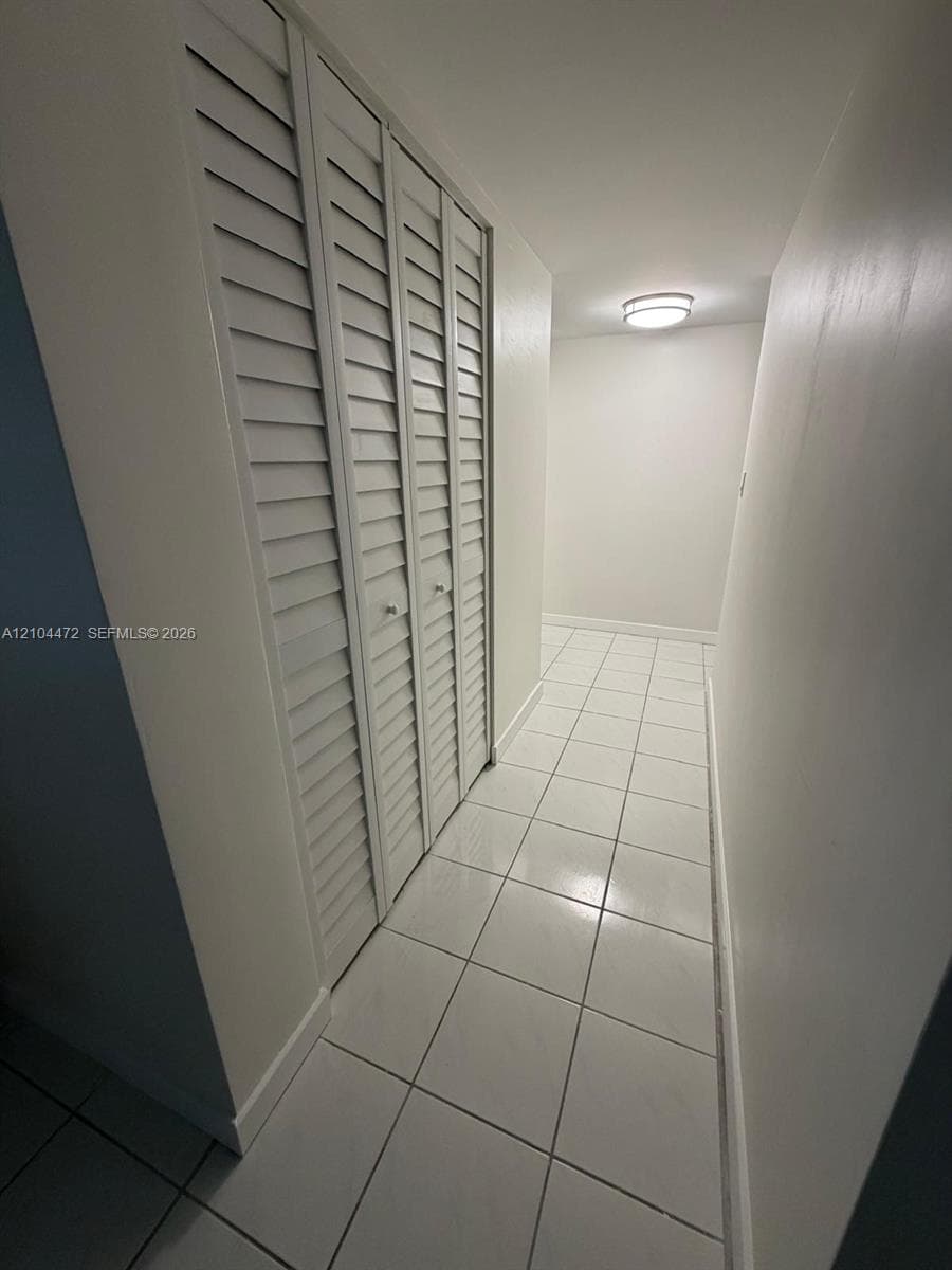 Hallway featuring white ceramic floor tiling, white louvered closet doors, and a flush-mount ceiling light fixture