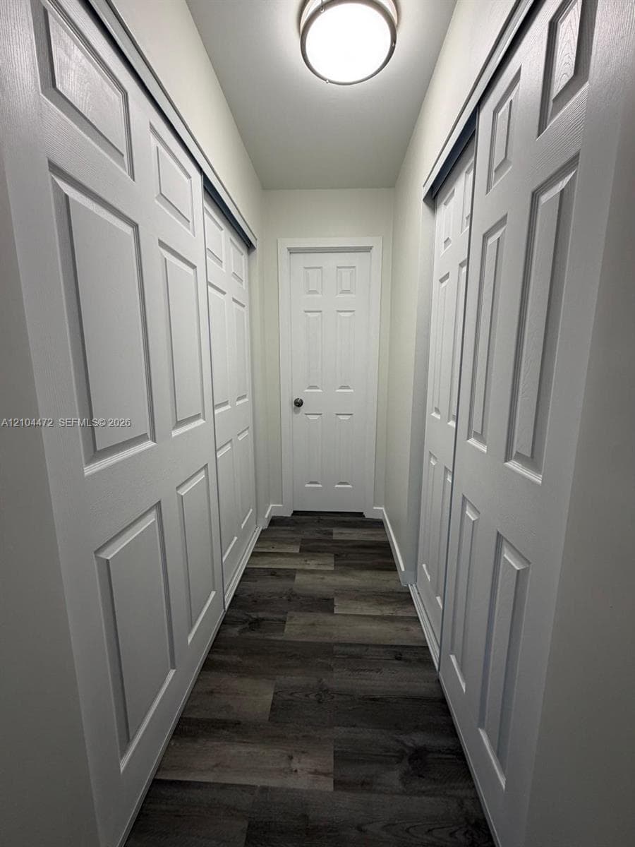 Hallway featuring wood-finish flooring, white six-panel doors, dual sliding closet doors, and a central flush-mount ceiling light fixture