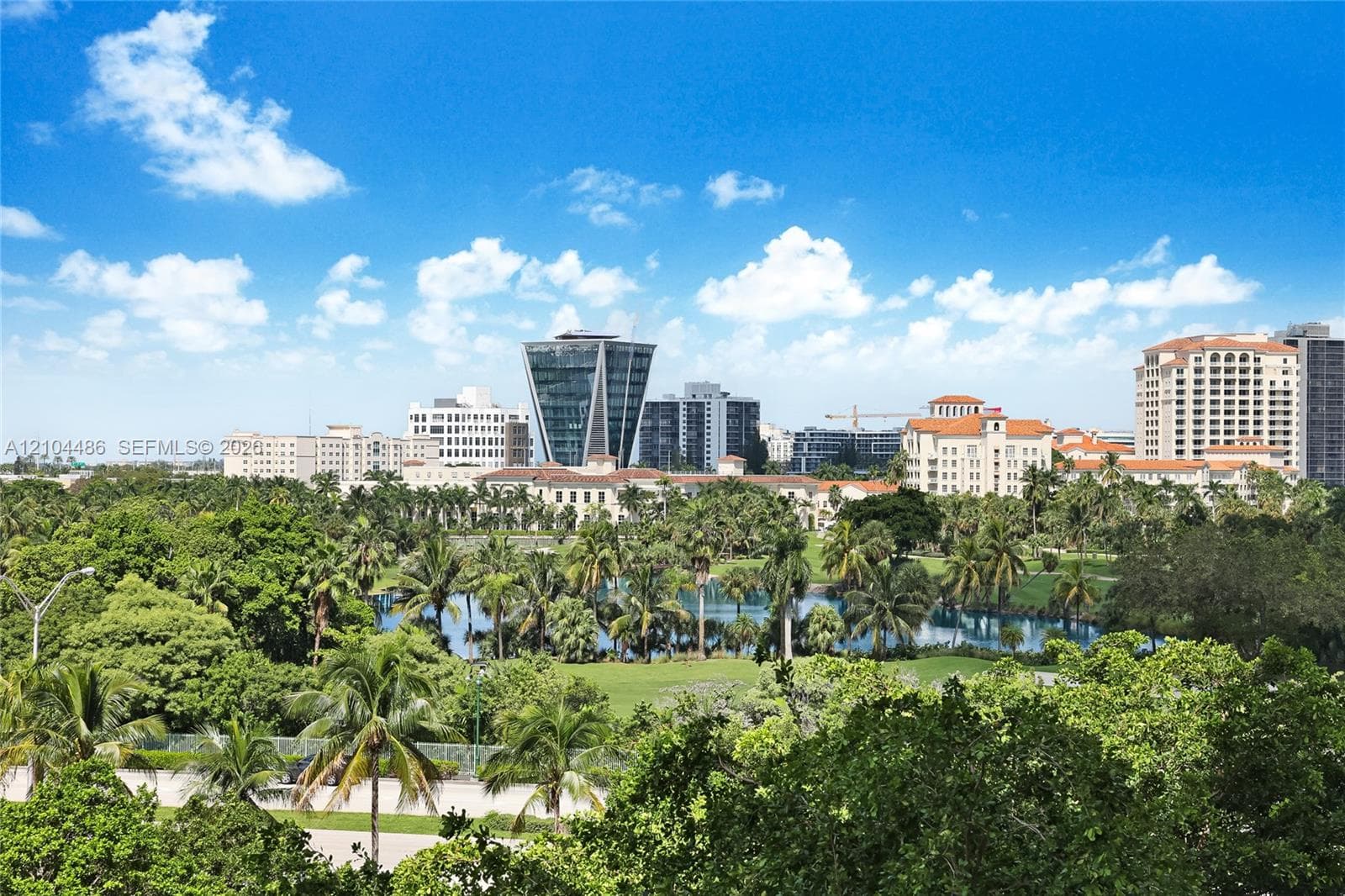 Elevated panorama featuring a lake, golf course, mature tropical landscaping, and a metropolitan skyline backdrop