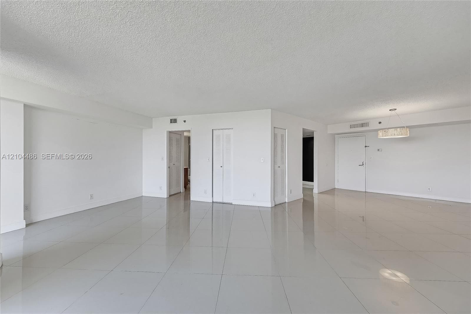 Open-concept interior featuring large-format polished tile flooring, smooth ceilings, bi-fold closet doors, and a circular drum chandelier