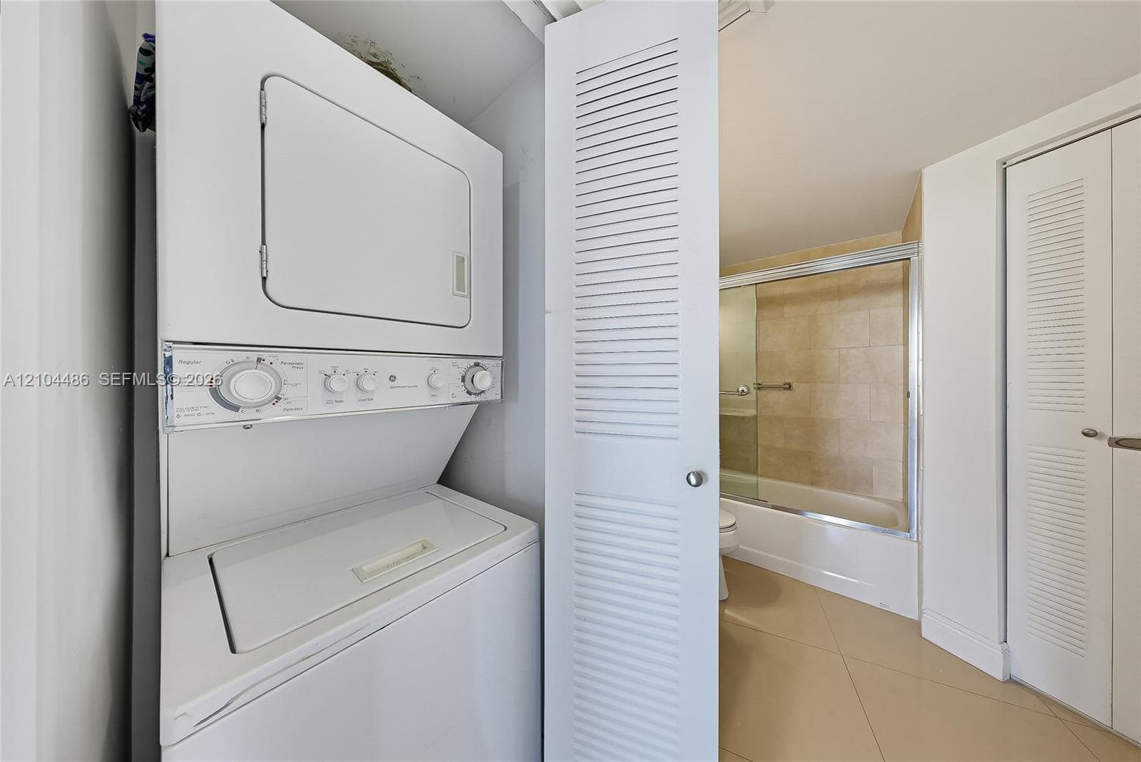 Laundry area featuring a stackable washer and dryer unit, white louvered closet doors, and tile flooring
