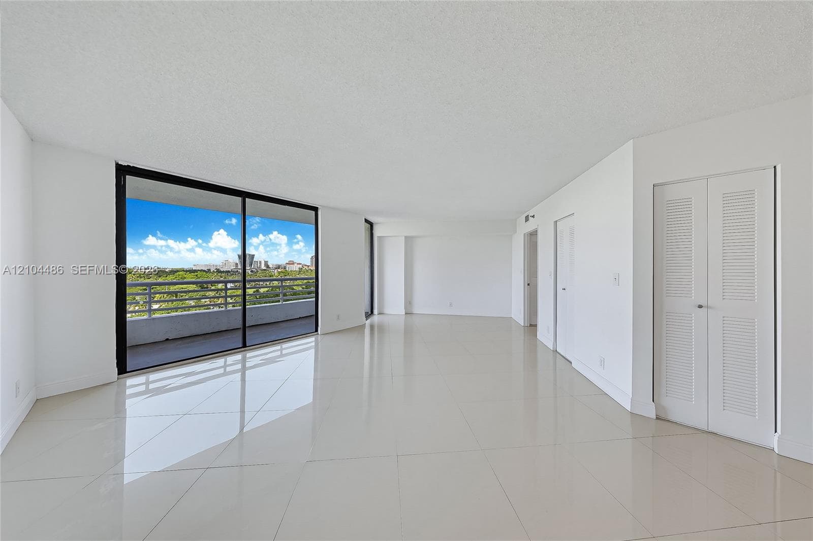 Open floor plan featuring large-format tile flooring, a floor-to-ceiling glass sliding door, an expansive private balcony, and built-in closet cabinetry