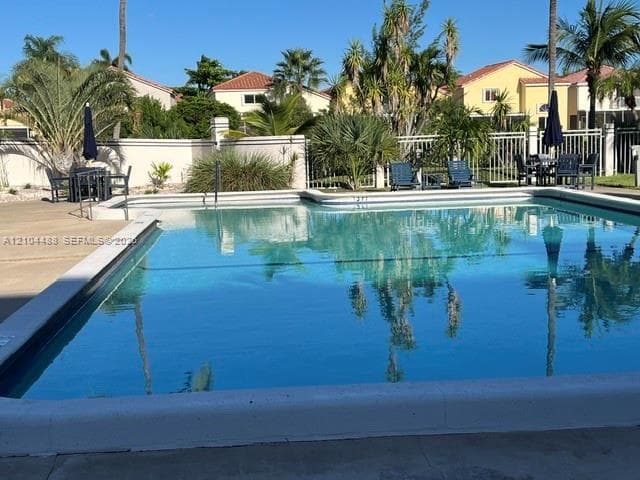 In-ground swimming pool featuring a concrete deck and perimeter metal fencing surrounded by mature palm trees and established landscaping
