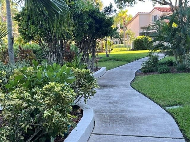 Concrete walkway flanked by manicured landscaping, mature trees, and a low-profile concrete retaining wall