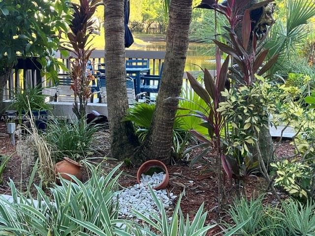 Landscaped garden featuring mature palms, varied tropical vegetation, and a decorative stone-filled accent bed, complemented by a wooden deck overlooking a pond