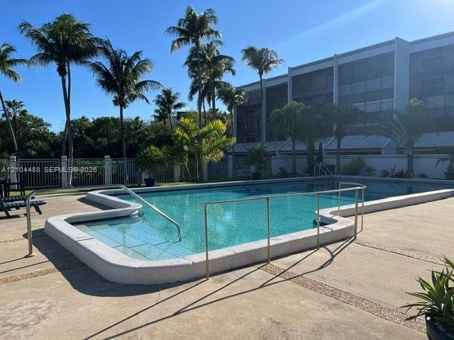 In-ground swimming pool featuring a concrete deck, metal safety railing, and integrated steps