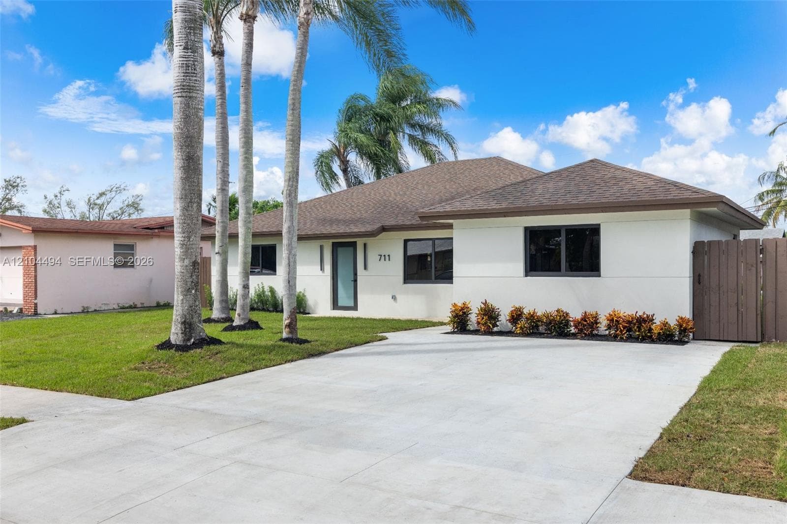 Single-story residence featuring a neutral stucco exterior, a concrete driveway, modern dark-framed windows, and a privacy fence