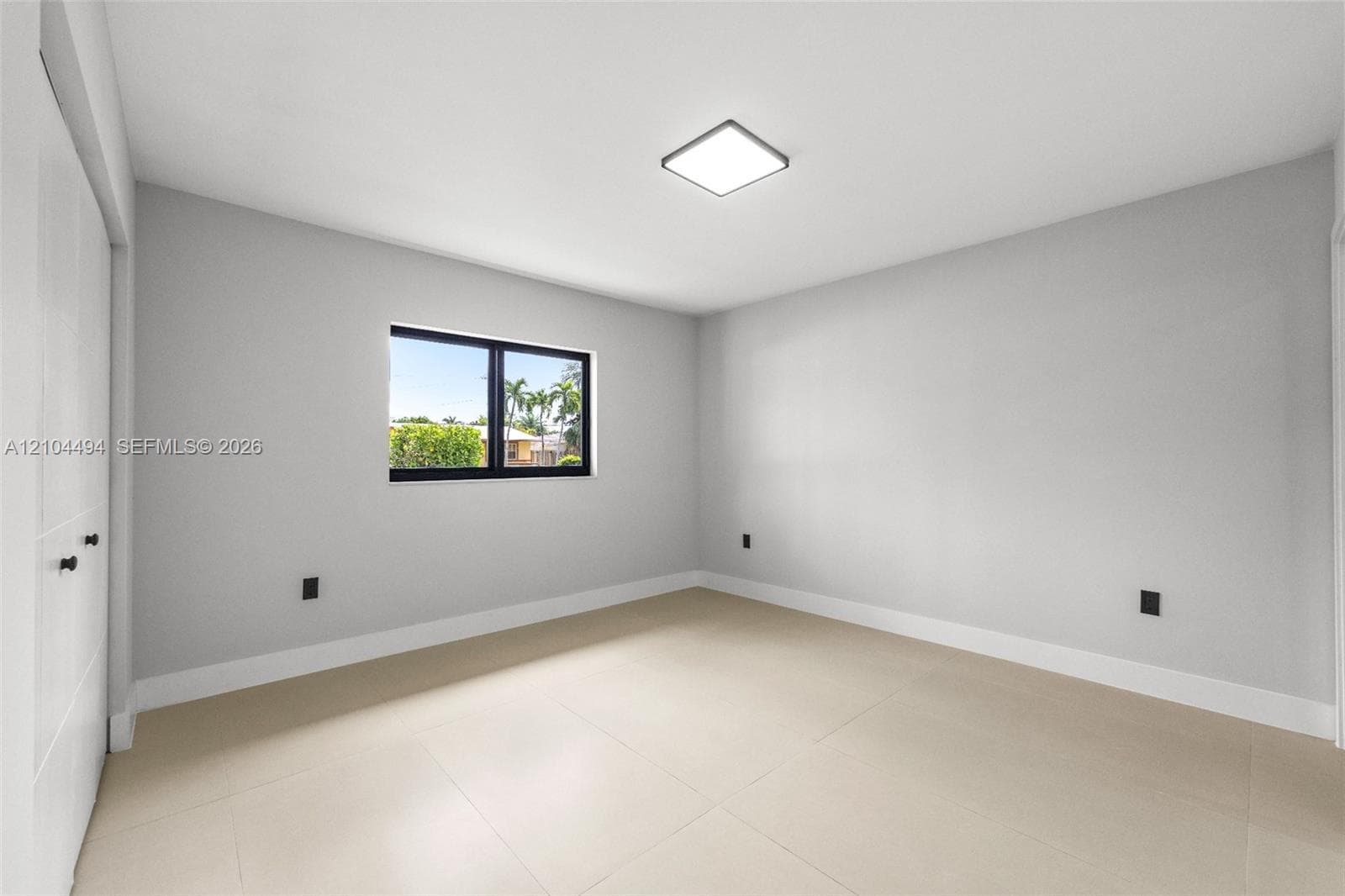 Neutral-toned interior featuring large-format tile flooring, recessed square ceiling lighting, and a window with a black frame
