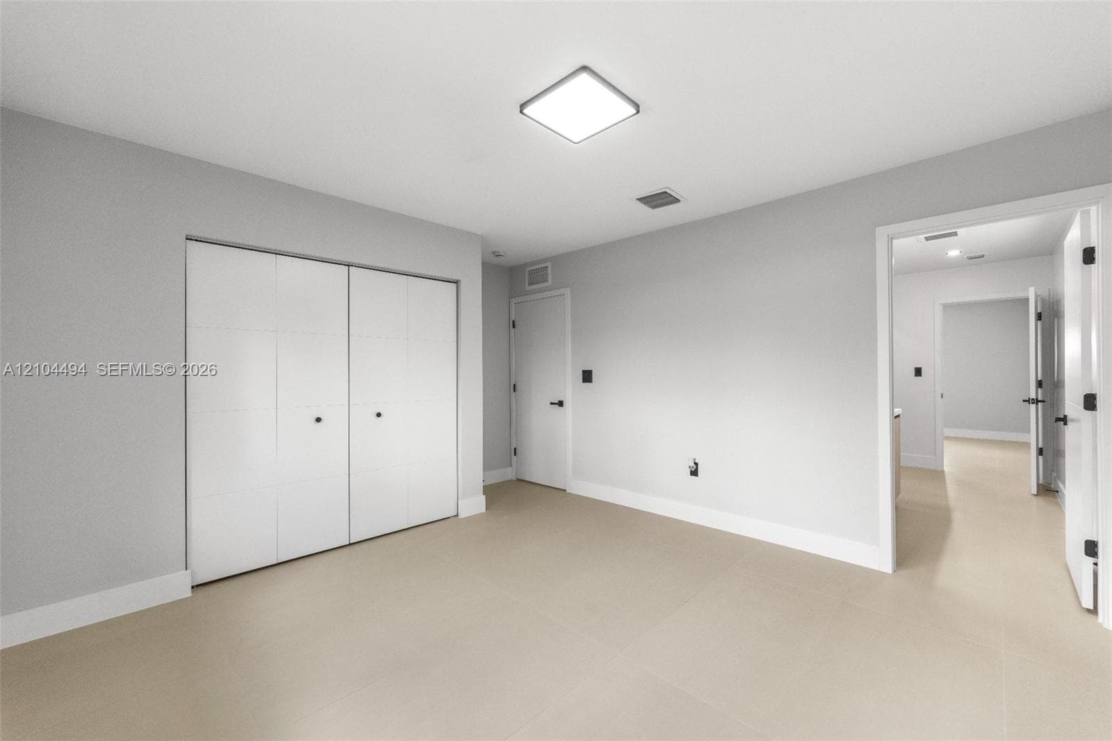 Neutral-toned room featuring large-format tile flooring, recessed square ceiling lighting, white flush-panel closet doors, and matte black door hardware