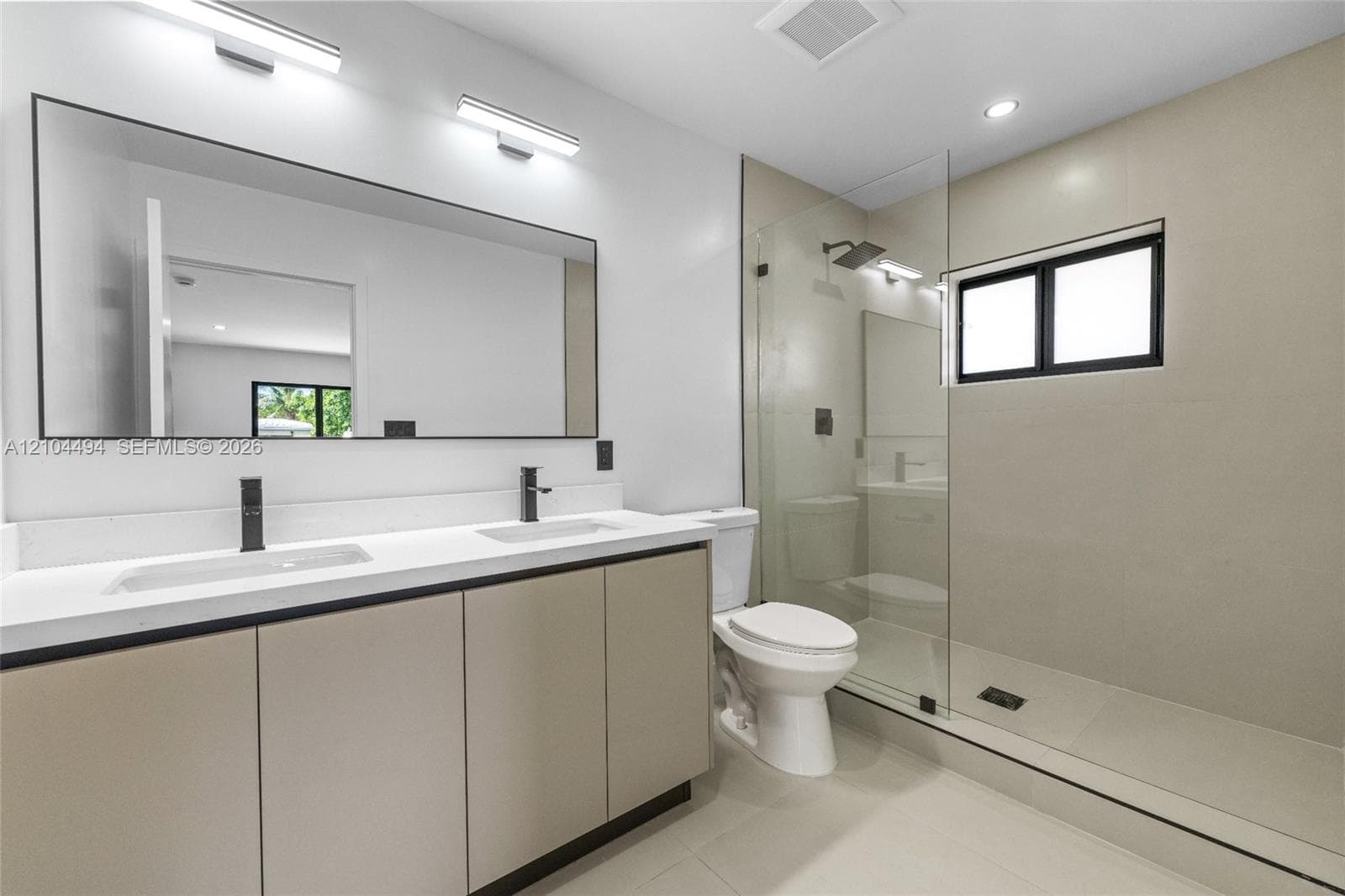 Dual-sink vanity with light-tone cabinetry and white countertop, large wall-mounted mirror, walk-in glass-enclosed shower, and matte black plumbing fixtures