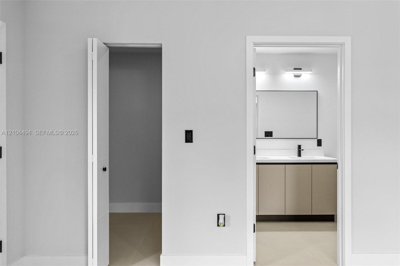 Bathroom featuring a double-sink vanity with light-toned cabinetry, a rectangular mirror with a dark frame, wall-mounted light fixtures, and a matte black faucet