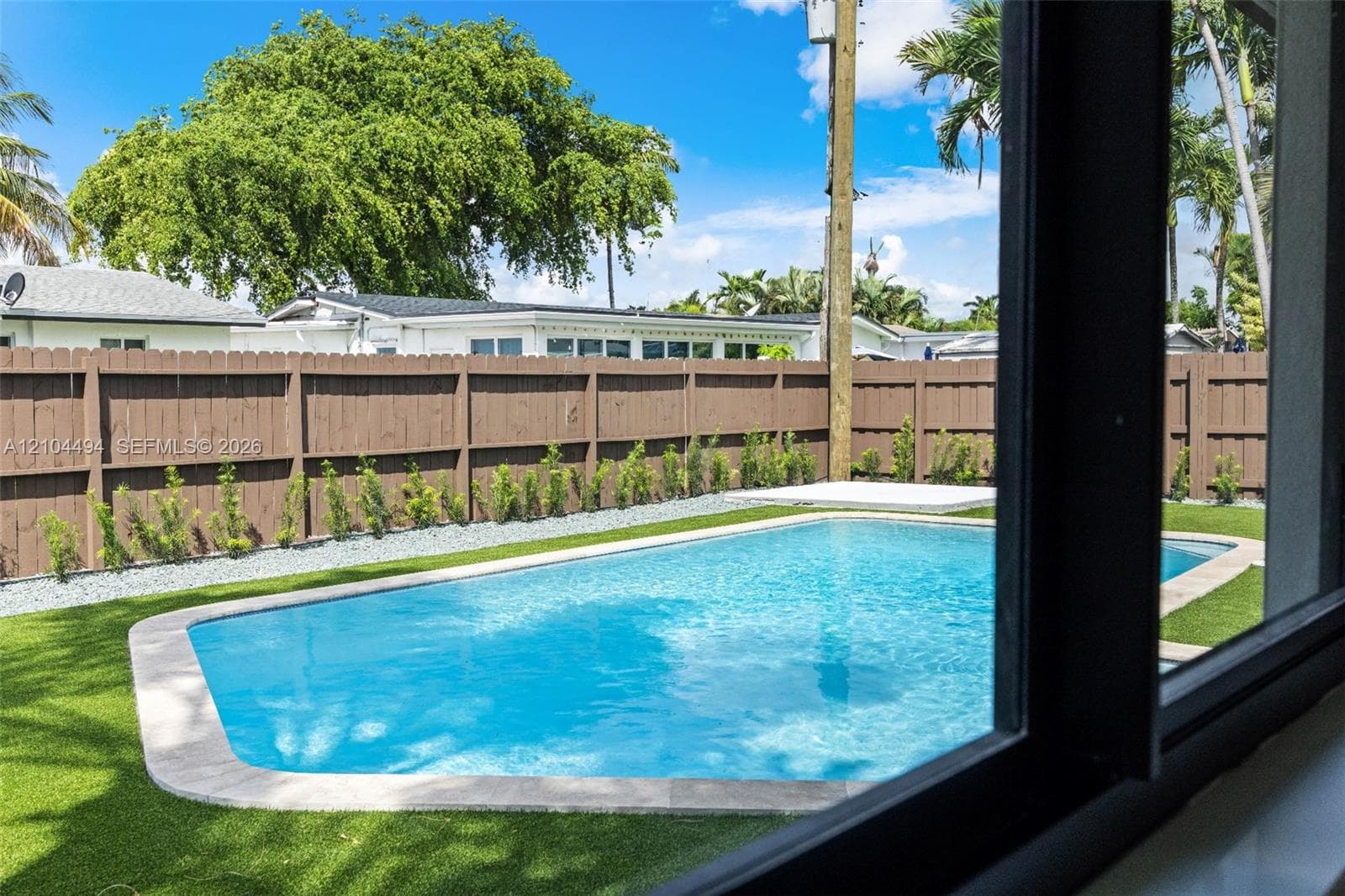 Outdoor space featuring a swimming pool with stone coping, synthetic turf lawn, wood privacy fencing, and perimeter landscaping