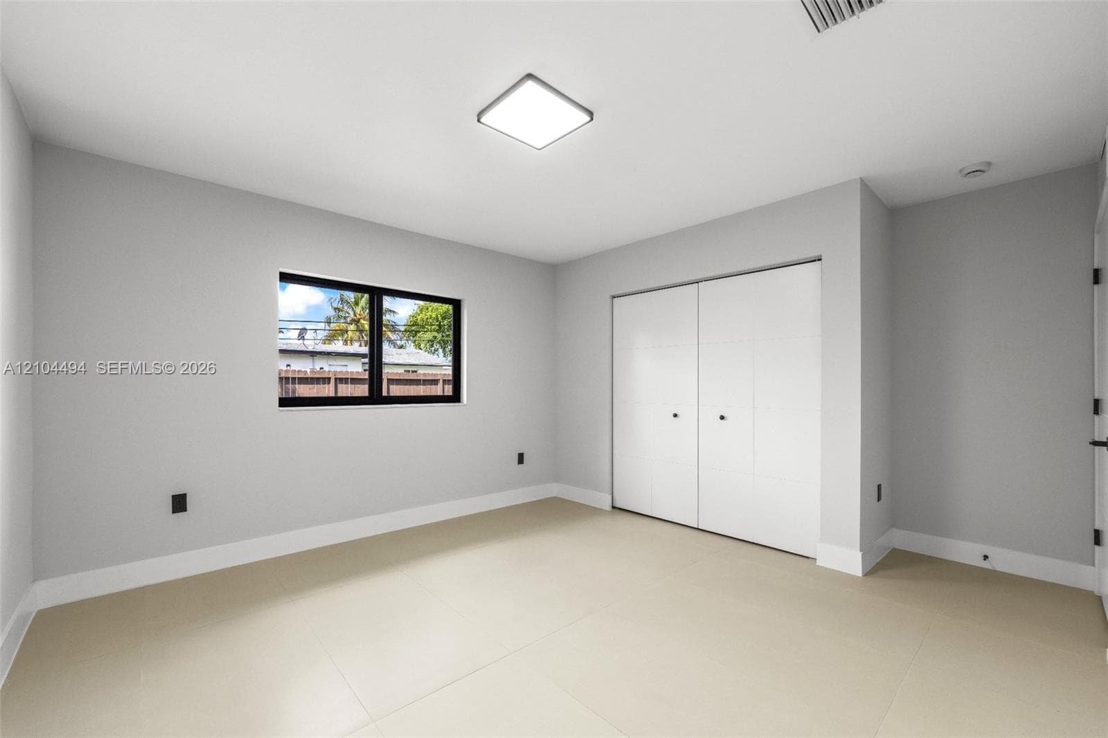 Neutral-toned room featuring large-format tile flooring, a square flush-mount LED fixture, a black-framed window, and a built-in closet with double doors