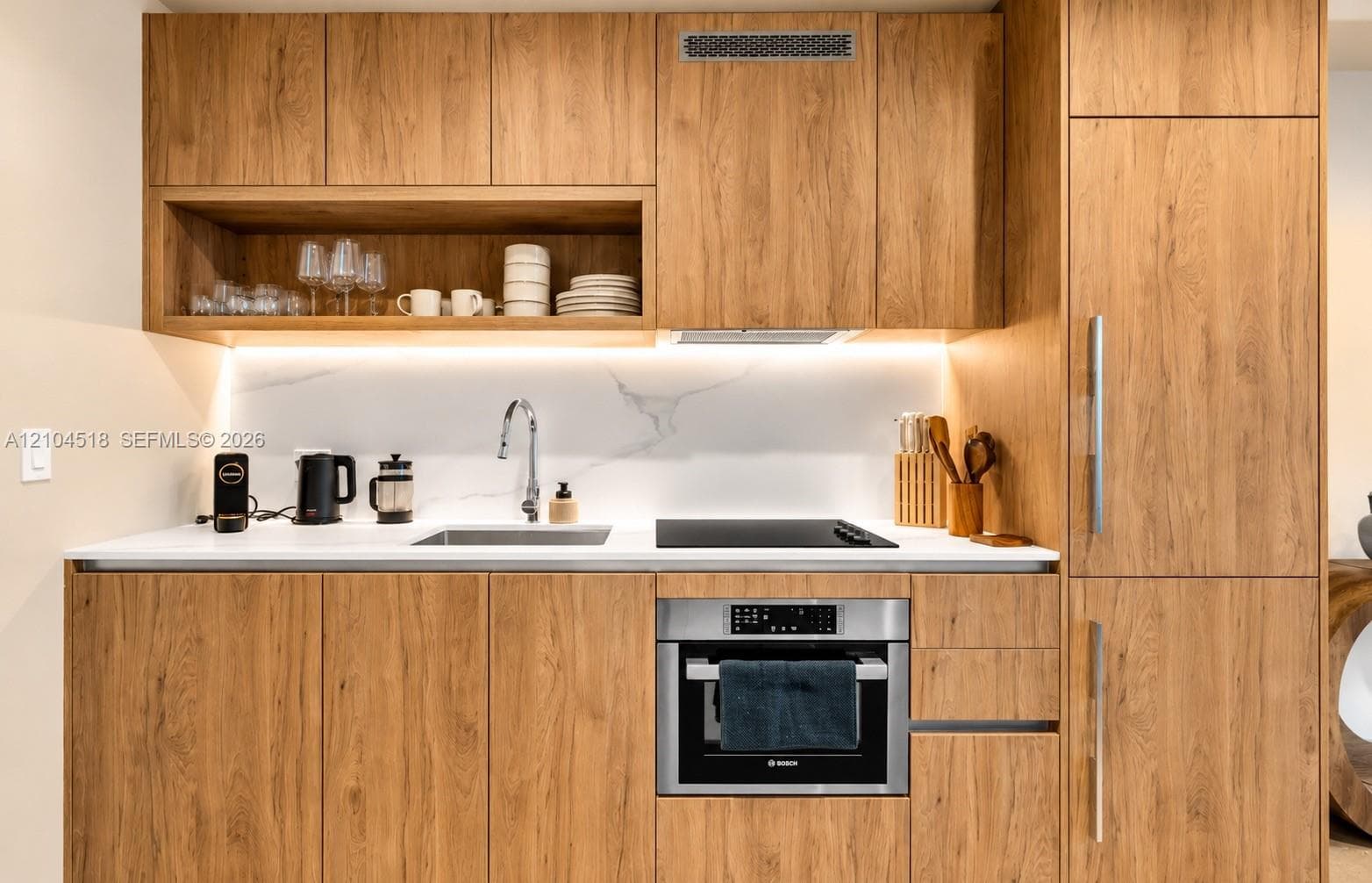 Full kitchen featuring wood-finish cabinetry, white countertop, white marble-finish backsplash, stainless steel sink, and integrated oven