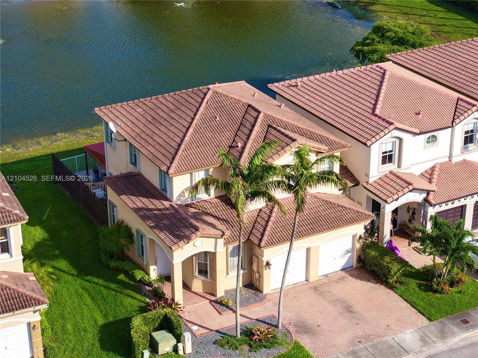 Two-story stucco exterior featuring a multi-gabled tile roof, paver driveway, two-car garage, and waterfront location