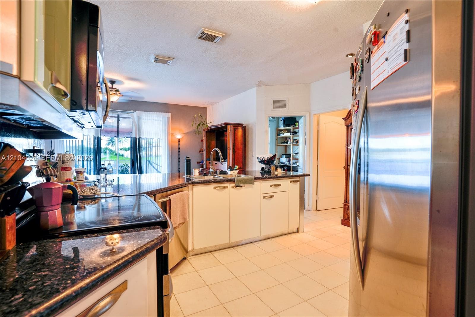 Kitchen featuring stainless steel appliances, dark stone-finish countertops, white cabinetry with metal hardware, and tiled flooring