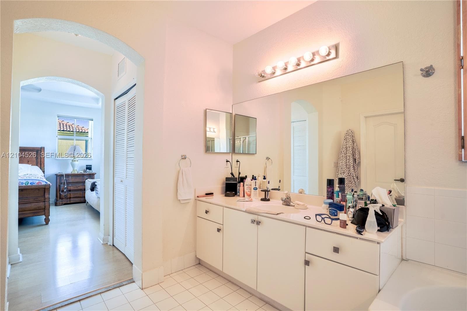 Bathroom featuring a white vanity cabinet with an integrated countertop and sink, wall-spanning mirror, multi-bulb vanity lighting, and arched architectural doorway