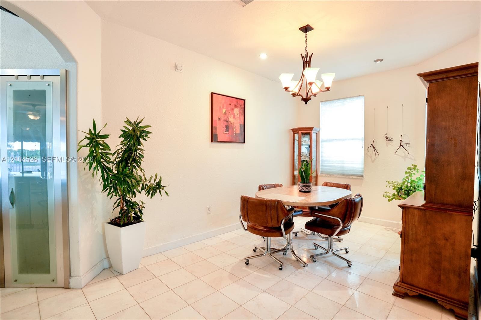 Light-filled room featuring large-format tile flooring, a multi-arm decorative chandelier, arched architectural detailing, and a door with frosted glass paneling
