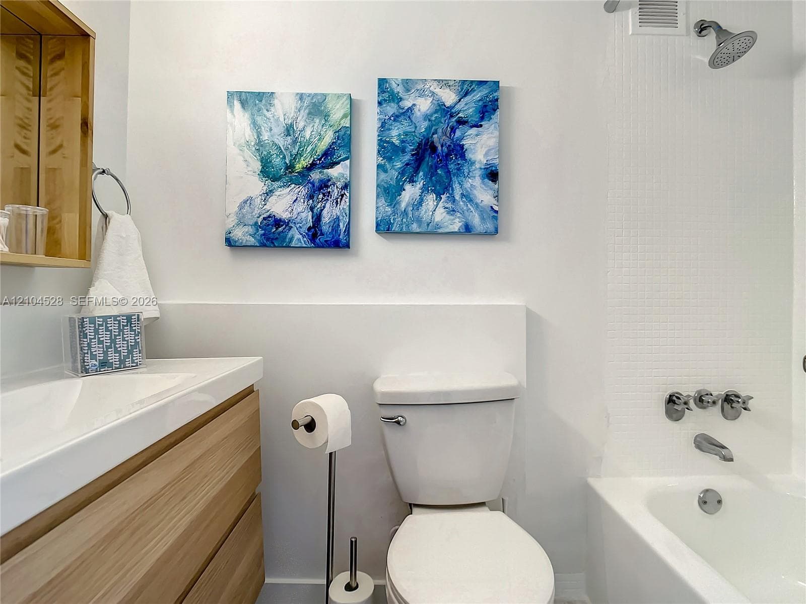 Bathroom featuring a wood-finish floating vanity, integrated rectangular sink, wall-mounted medicine cabinet, and a tiled shower-tub combination with chrome fixtures