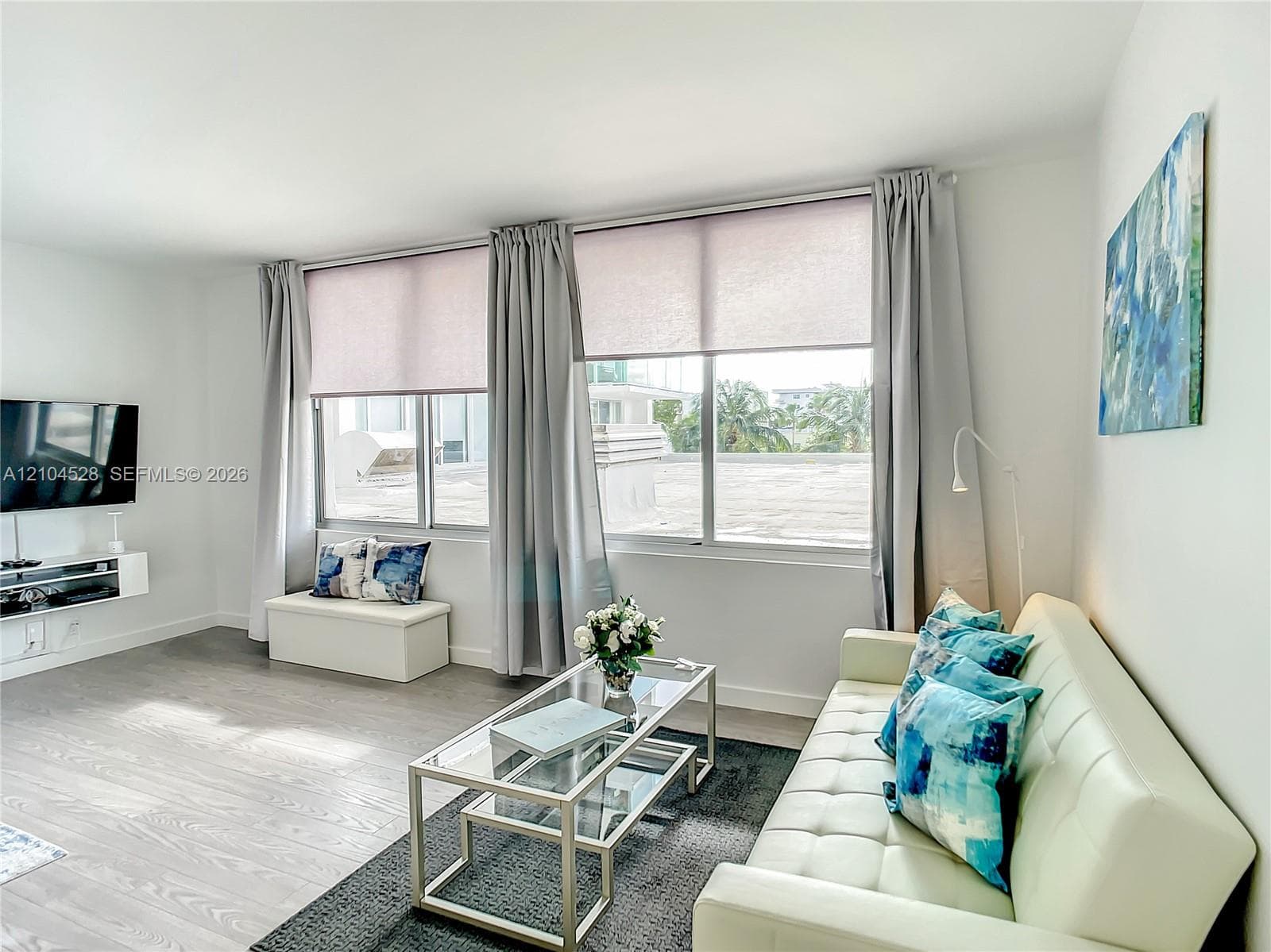 Neutral wall-to-wall wood-finish flooring, expansive windows with integrated roller shades, and a wall-mounted floating media console
