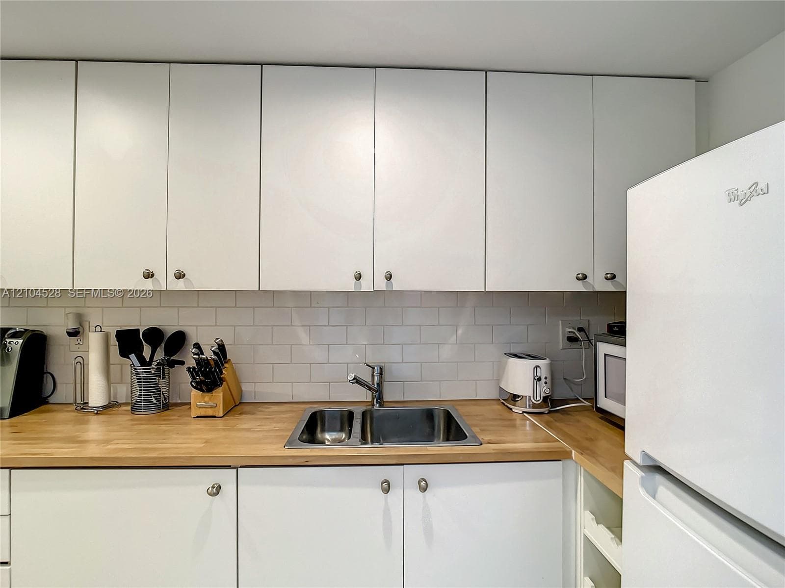 Kitchen featuring white flat-panel cabinetry, light wood-finish countertops, stainless steel dual-basin undermount sink, and white subway tile backsplash