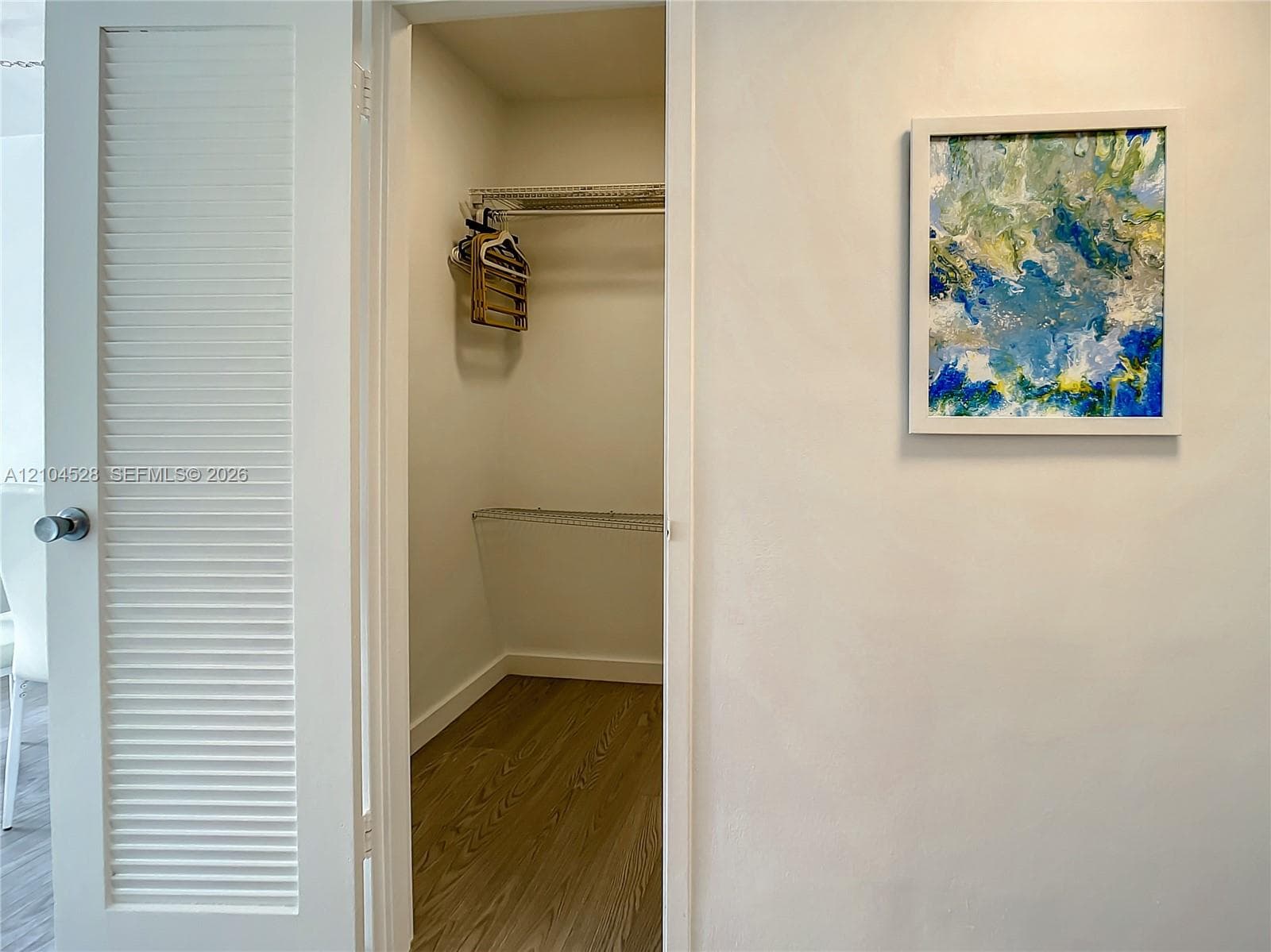 Louvered interior door with a circular knob opening to a storage space featuring wire shelving and wood-finish flooring
