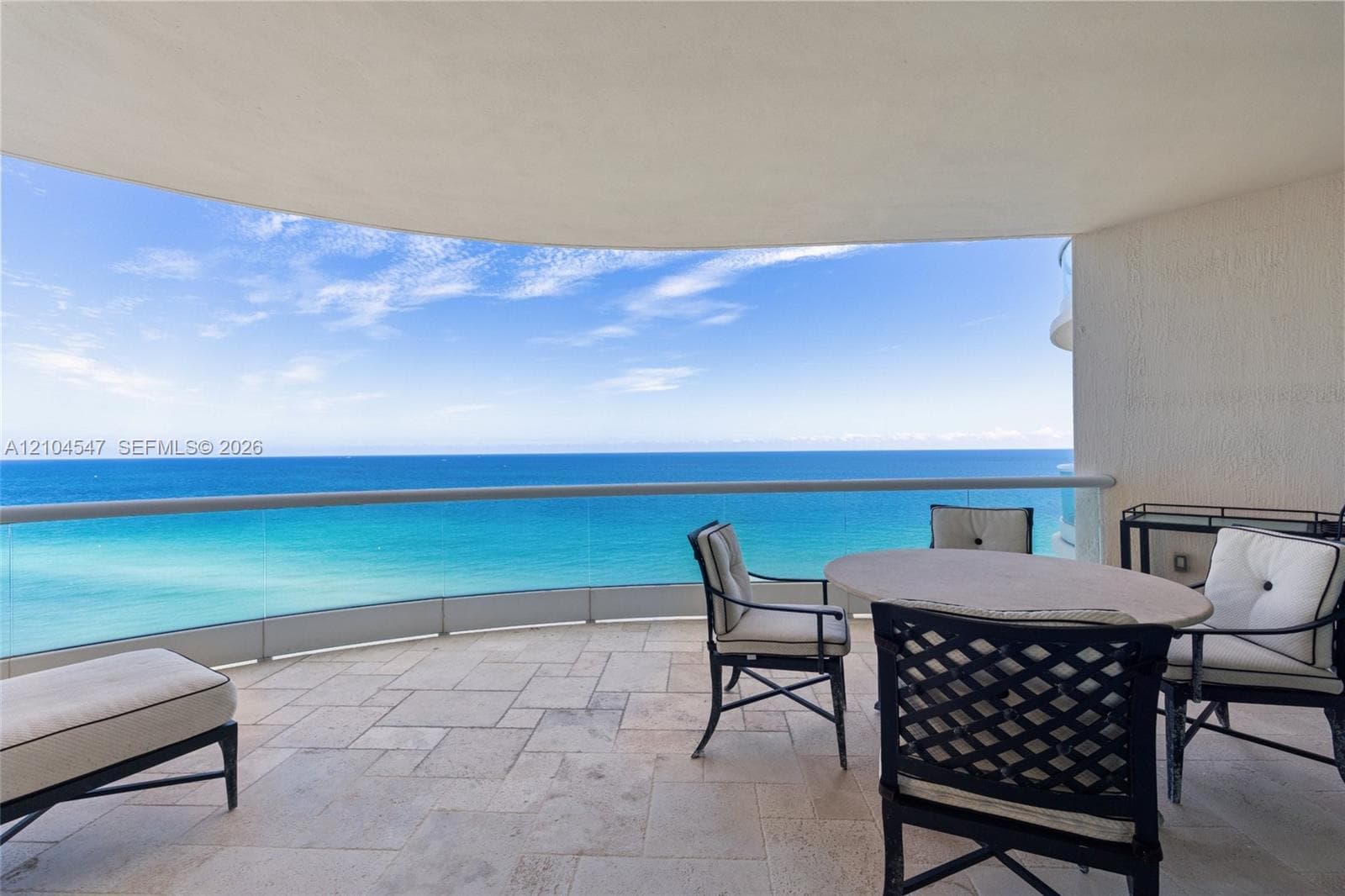 Covered balcony featuring stone-tile flooring and a transparent glass panel railing overlooking the ocean