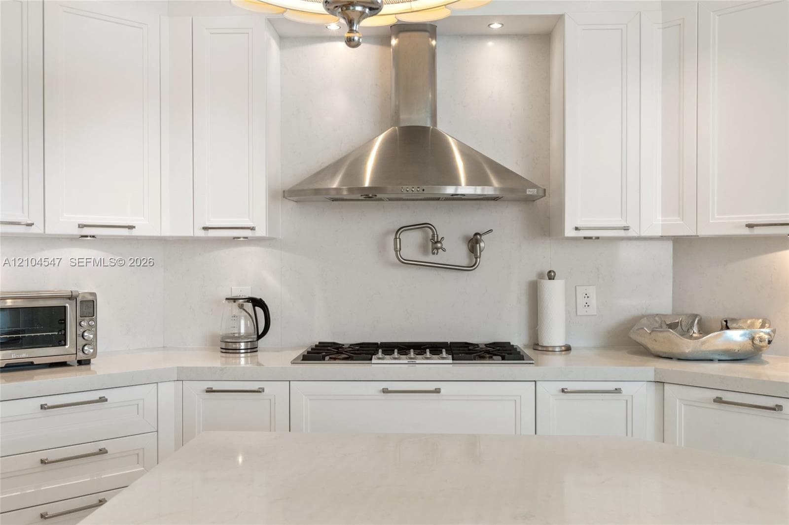Kitchen featuring white shaker-style cabinetry, quartz countertops, a stainless steel gas cooktop, a wall-mounted pot filler, and a stainless steel vent hood