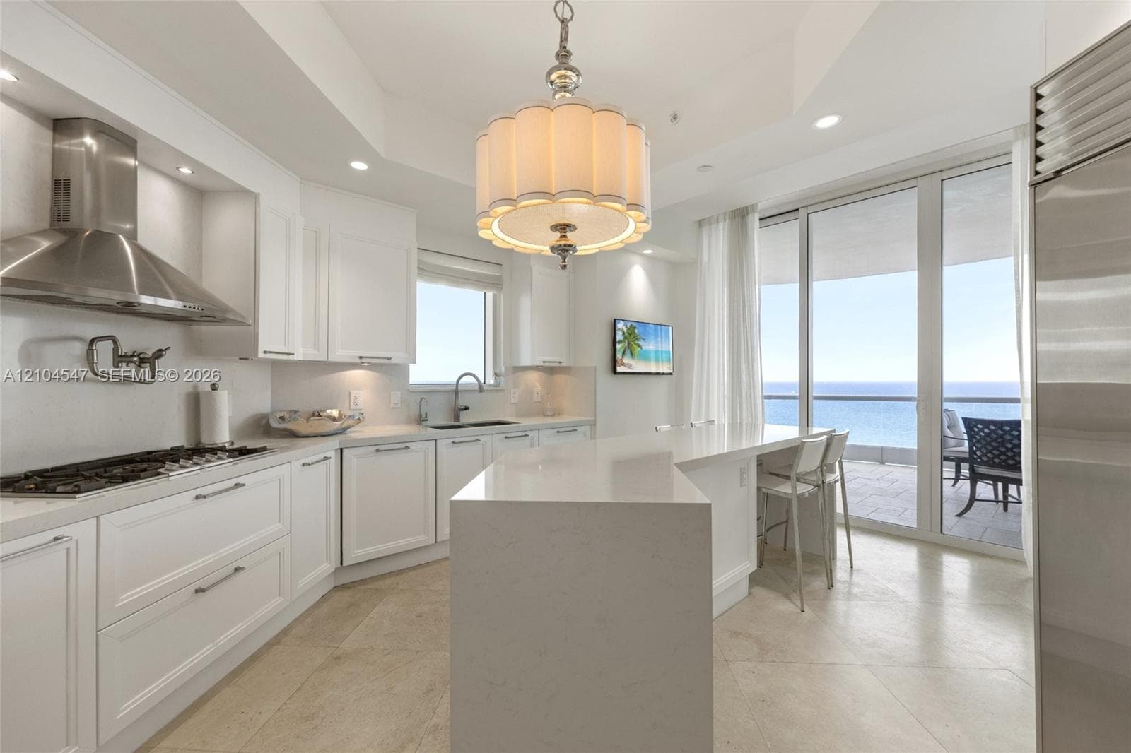 Kitchen featuring white cabinetry, stone countertops, central island with seating, stainless steel appliances, and floor-to-ceiling glass sliding doors