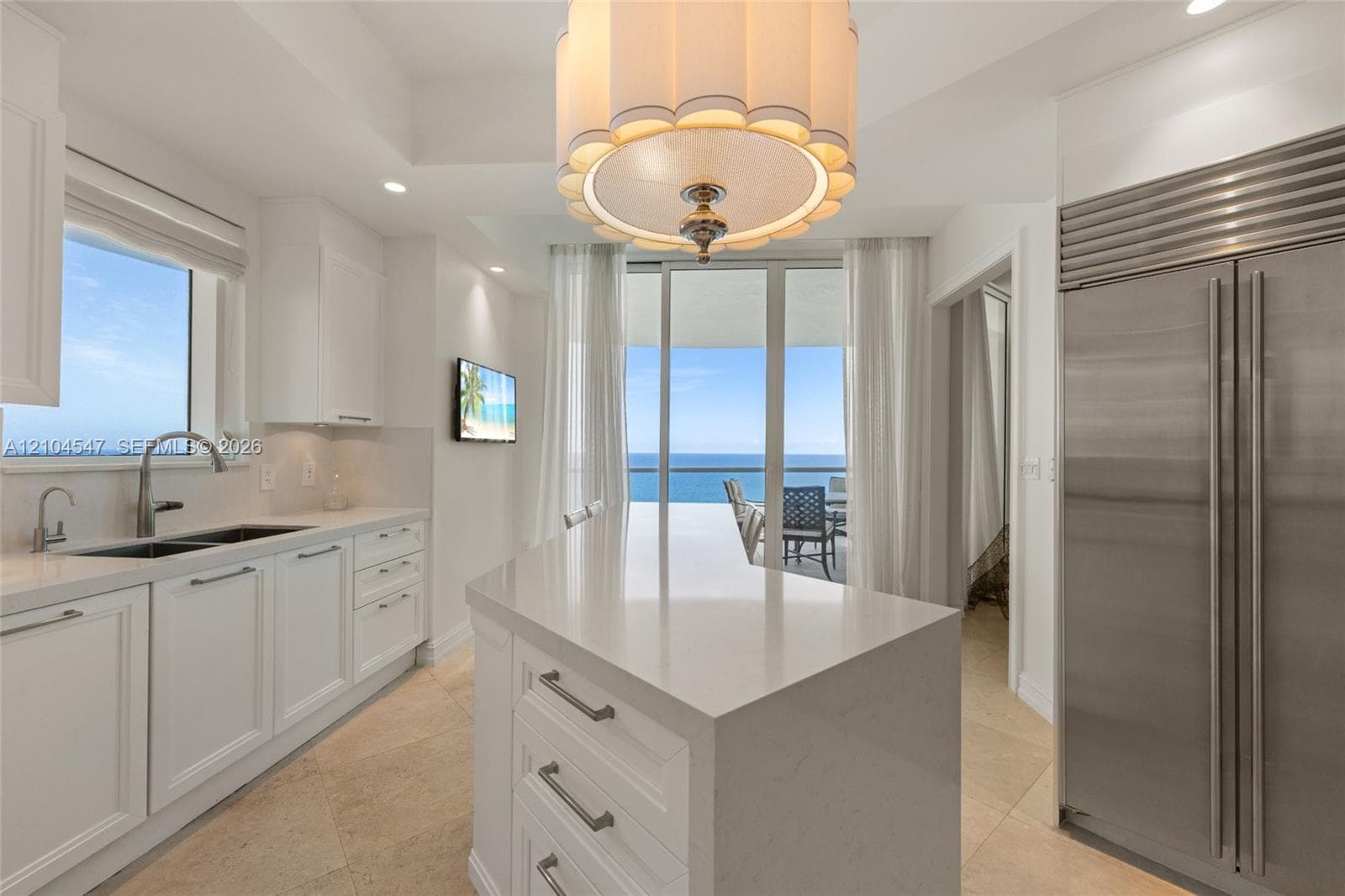 Kitchen featuring an expansive center island with quartz countertops, custom white shaker-style cabinetry, professional-grade stainless steel refrigerator, and a decorative drum pendant light fixture over the island