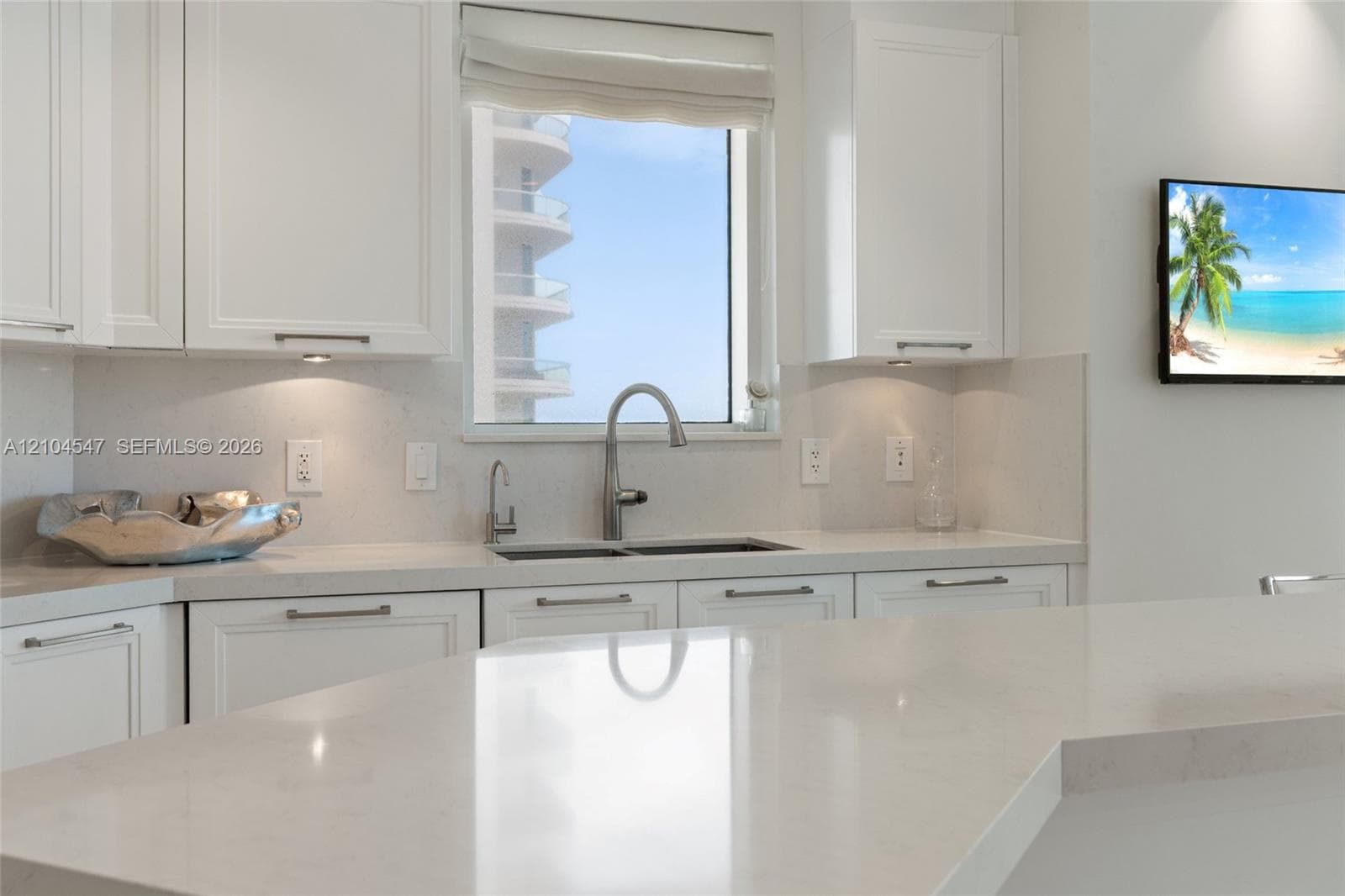 Kitchen featuring white shaker-style cabinetry, solid-surface countertops, dual-basin stainless steel sink, gooseneck faucet, and under-cabinet lighting