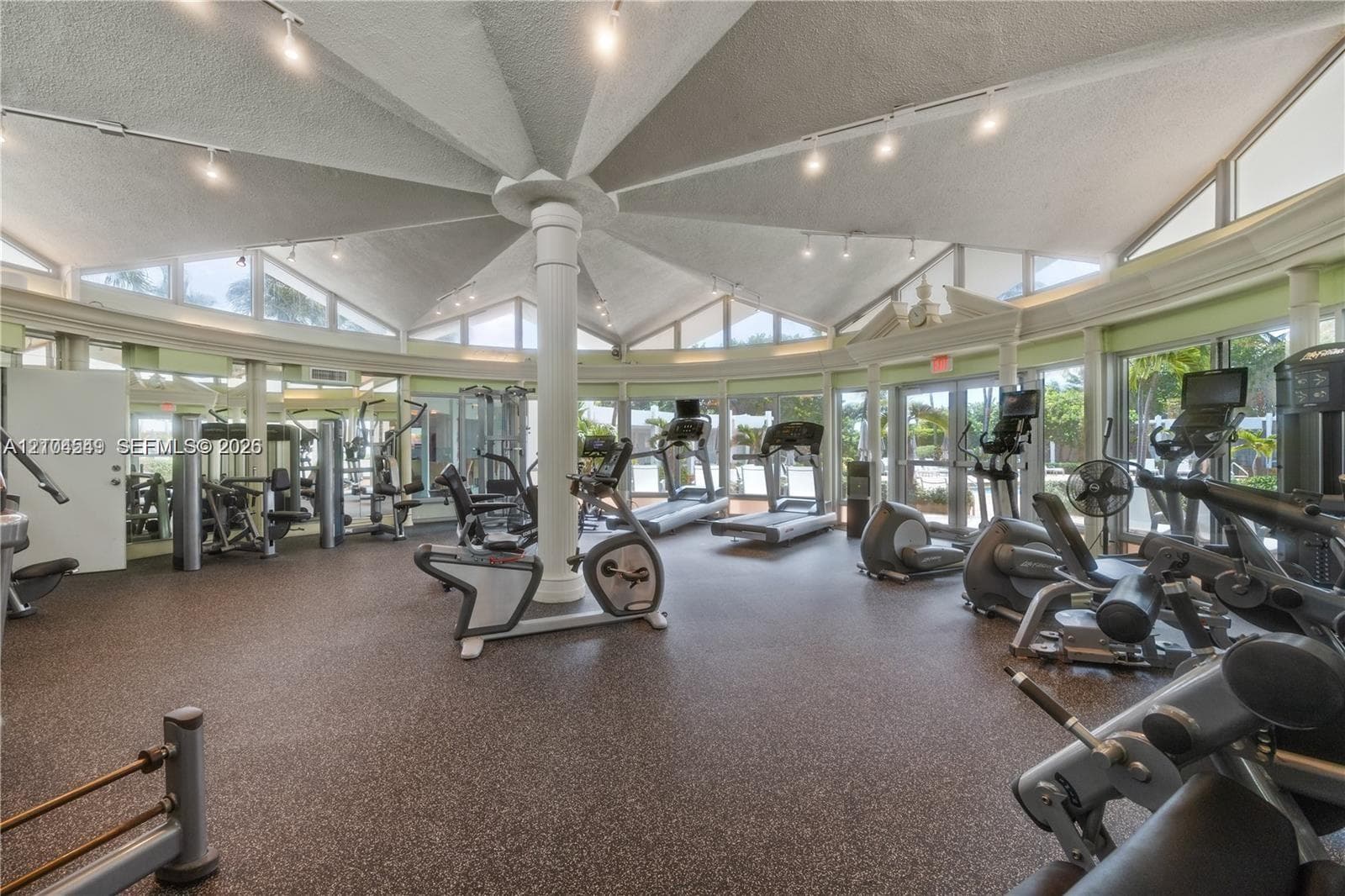 Spacious fitness center featuring a radial vaulted ceiling, extensive window line, and a resilient rubberized floor