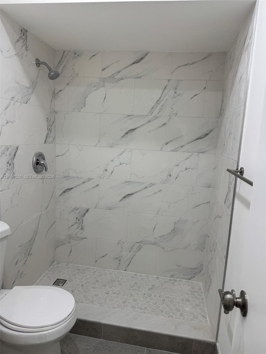 Walk-in shower featuring large-format white stone-finish tile surround, pebble-texture floor tiling, and chrome wall-mounted fixtures