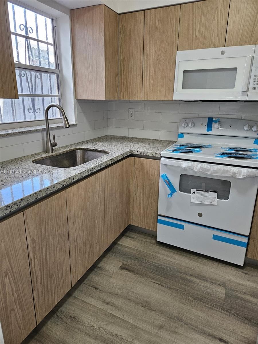 Kitchen featuring wood-finish cabinetry, stone-surface countertops, subway tile backsplash, stainless steel undermount sink with a gooseneck faucet, and wood-finish flooring