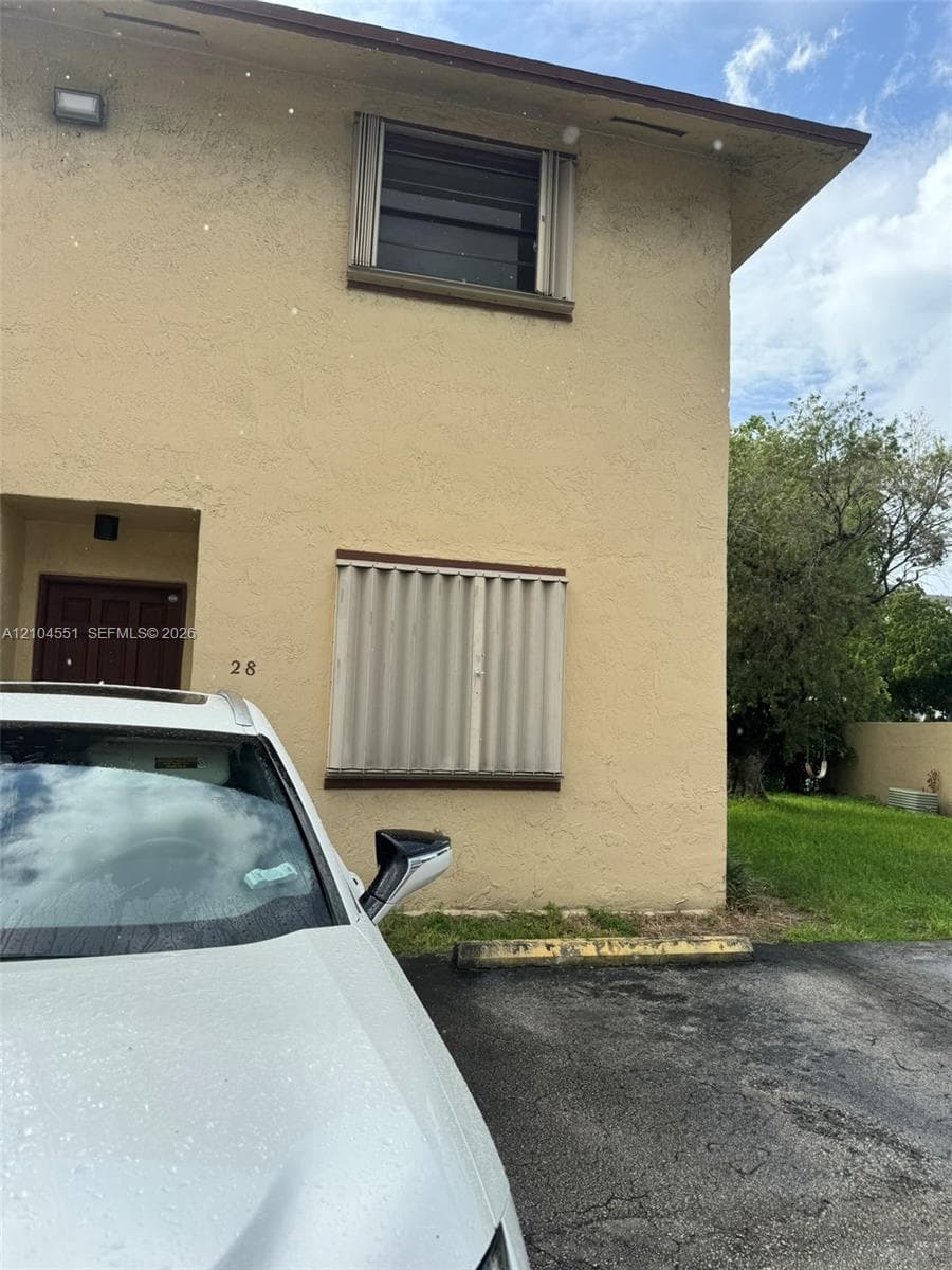 Stucco exterior featuring accordion-style hurricane shutters, recessed entryway, and asphalt surface parking